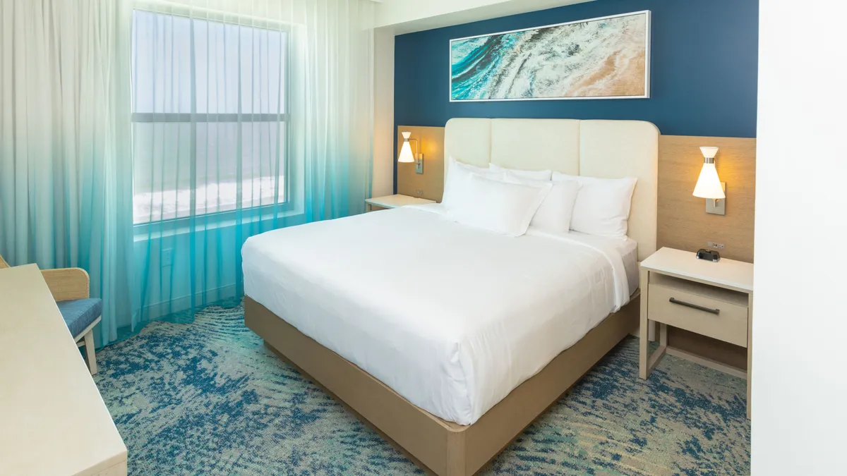 A tranquil bedroom featuring a large, comfortable bed positioned to take advantage of the soft morning light filtering through sheer curtains. Tasteful artwork and well-placed lamps on nightstands add to the peaceful, upscale ambiance.